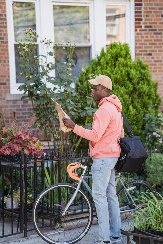 A bicycle courier in pink hoodie delivers a package in a residential urban area.